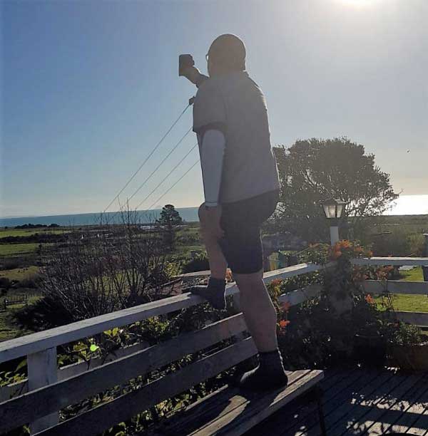 Kirk Mariner is standing on the edge of a deck holding up his phone in search of reception.