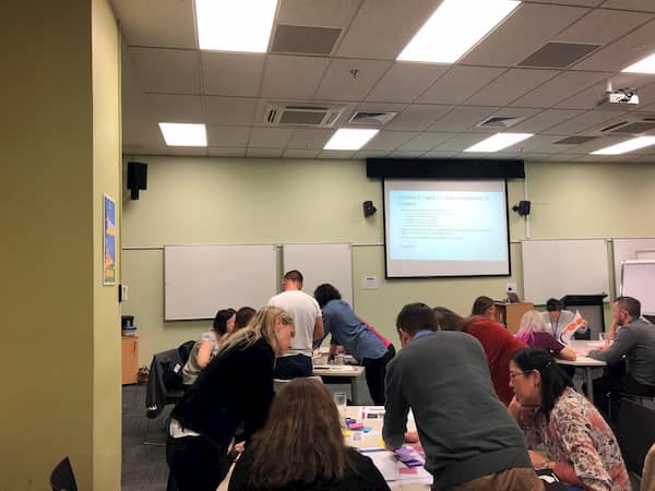 View from back of room of participants seated at tables working on group exercise.