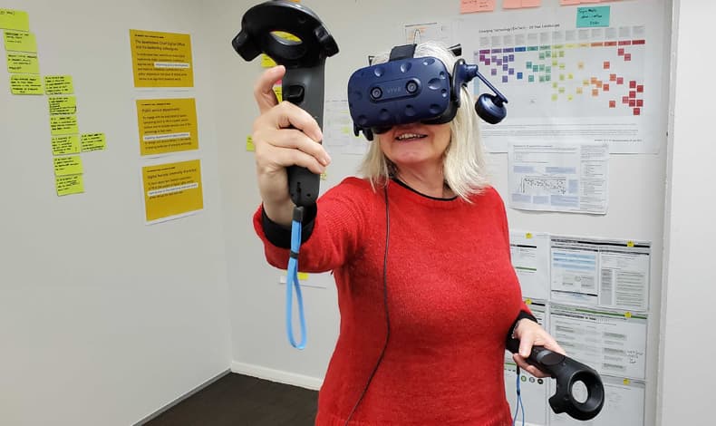 A woman wearing a virtual reality headset and using hand controllers to interact with the environment.